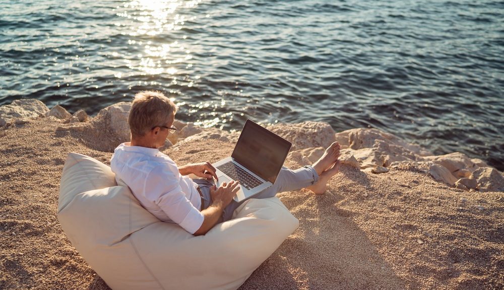 Man met laptop aan het strand
